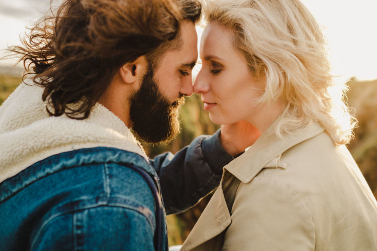 Bearded man touching noses with blond girlfriend during romantic date on weekend day in countryside in aviles, spain