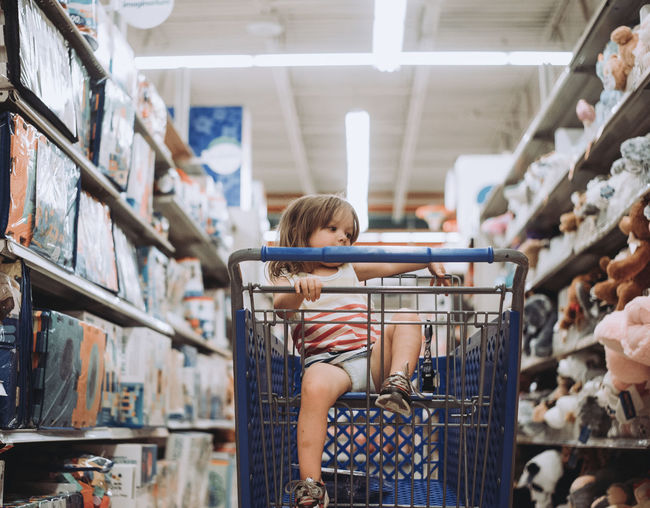 Playful girl sitting in shopping cart at supermarket