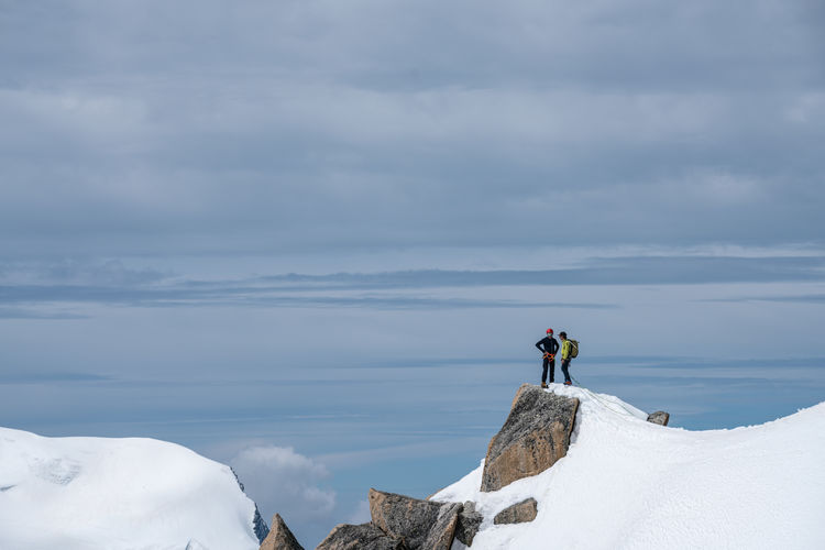 Friends standing on snowcapped mountain against sky