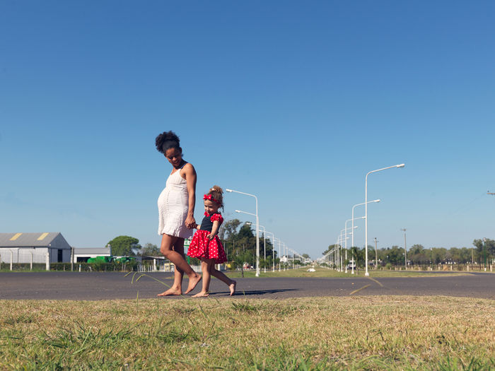 Pregnant mother and daughter walking on land against sky