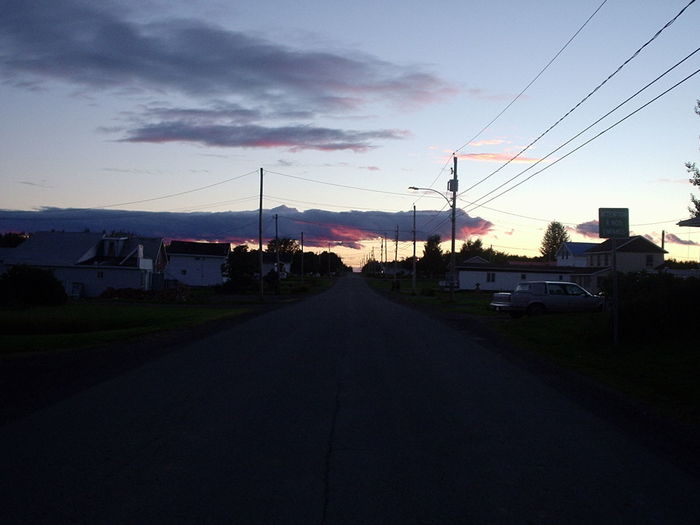 Road by houses against sky during sunset