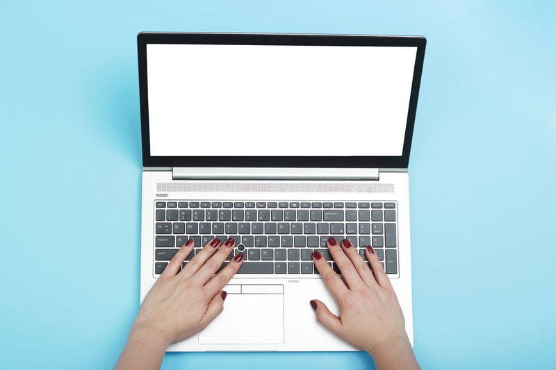 Female hands with red manicure are typing on laptop a blue background top view.