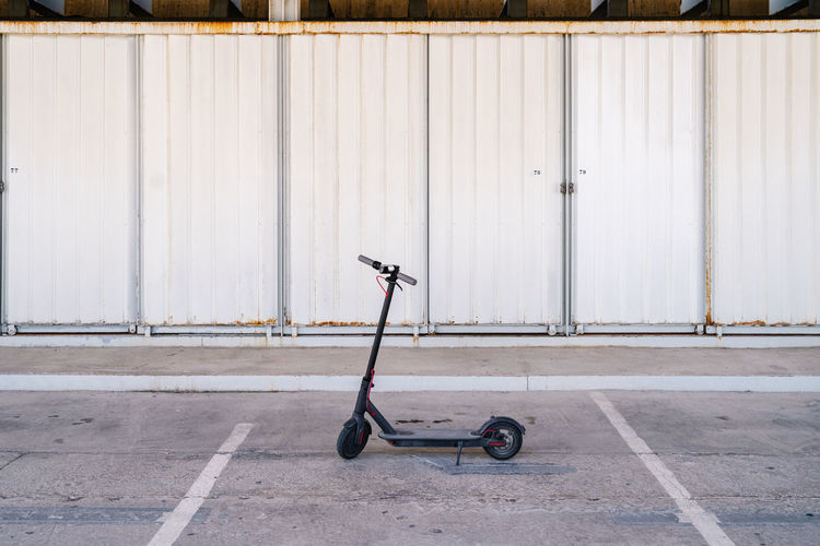 Modern electric scooter placed on paved parking lot against metal wall of urban building