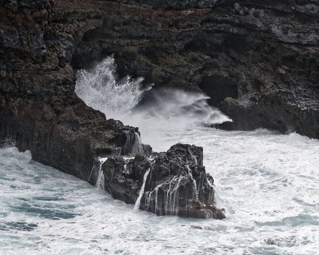 A wave breaks in stormy weather on a rocky coast with a small bay, canary islands, la palma