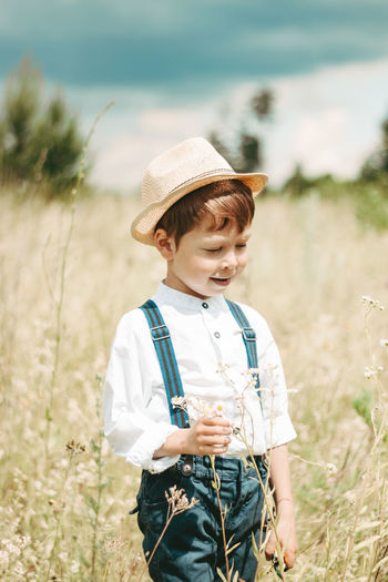 Little farmer on a summer field, cute little boy in a straw hat. boy with a flower 