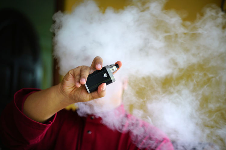 Close-up of man holding electronic cigarette amidst smoke