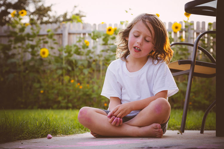 Cute girl sitting by chalk in yard