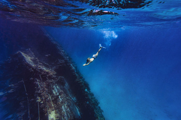 Woman diving underwater near shipwreck in sea
