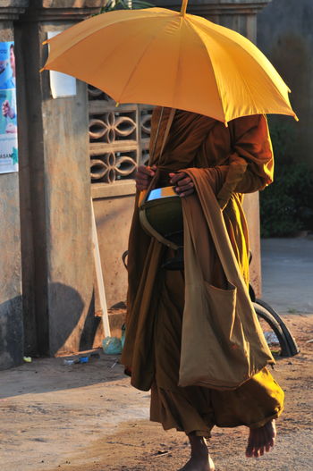 Monk carrying umbrella while walking on street