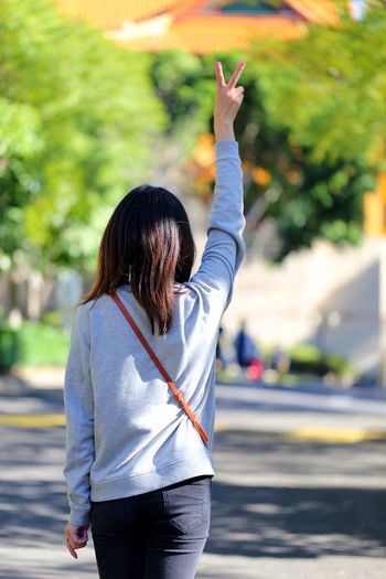 Rear view of young woman showing peace sign on road