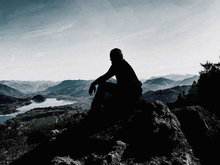 Silhouette man sitting on rock against sky