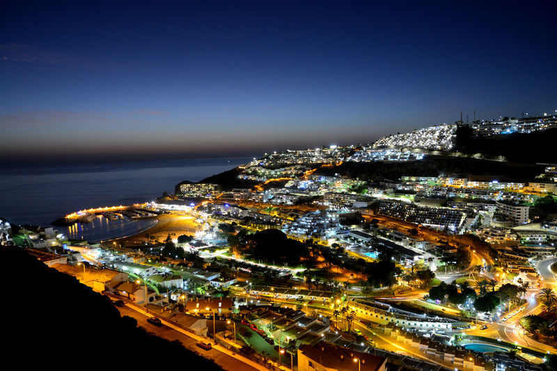 High angle view of illuminated city by sea against clear sky