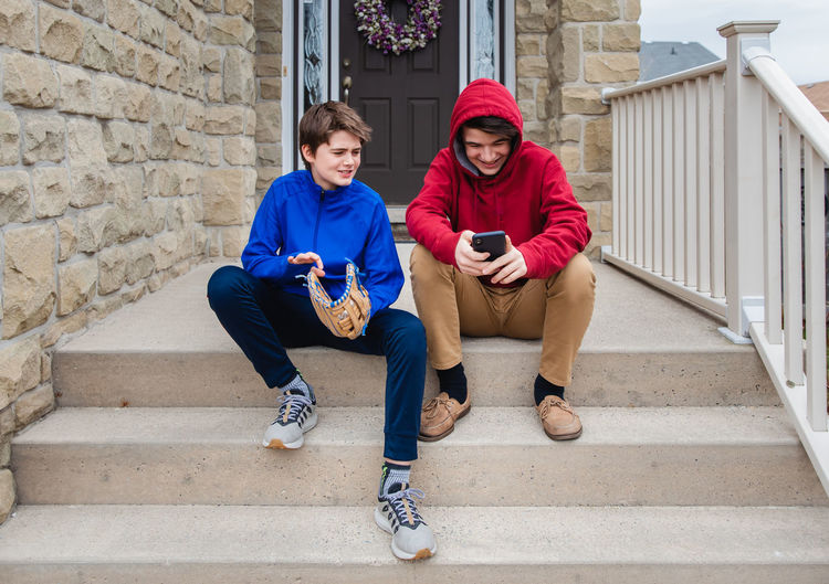 Two teenage boys sitting and talking on the front steps of a house.
