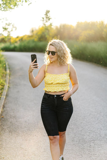 Young woman using phone while standing on road