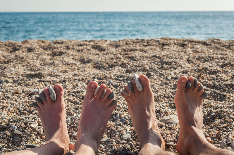 Low section of couple with pebbles sitting at beach