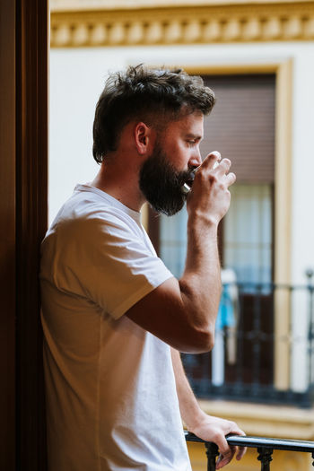 Bearded guy with hot drink resting on balcony