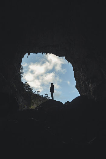 Low angle view of silhouette woman standing on cliff against sky