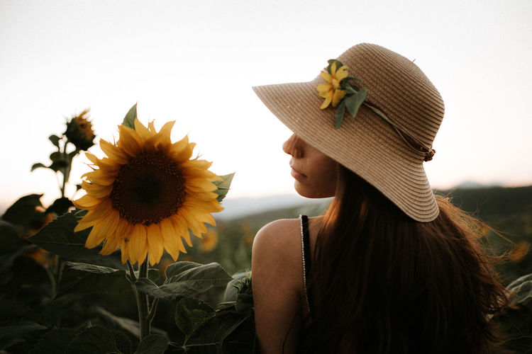 Woman by sunflower plants against sky