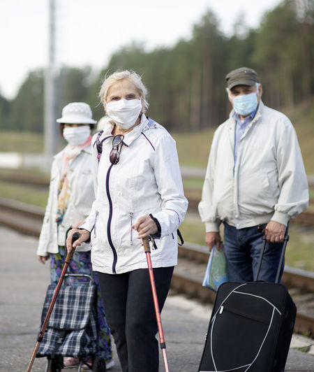 Group of elderly seniors people with face masks waiting train before traveling during a pandemic