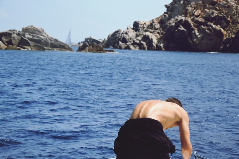 Rear view of shirtless man on boat in sea against sky