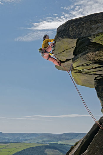 Side view of man climbing on rock against sky