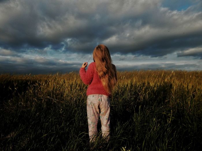 Rear view of woman on agricultural field against cloudy sky