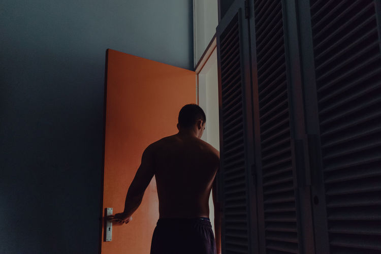 Rear view of shirtless man standing at doorway