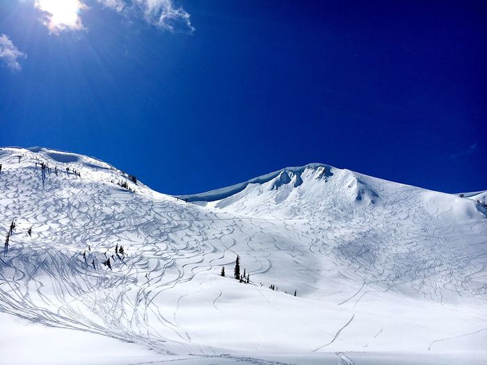Low angle view of ski tracks on snowcapped mountains against blue sky