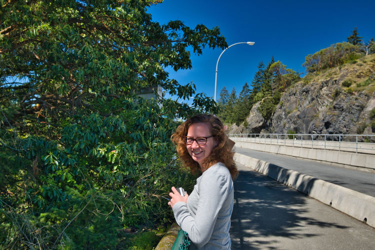 Portrait of smiling woman by trees against road