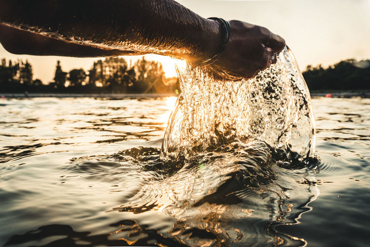 Cropped hands of man splashing water during sunset