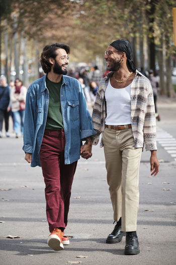 Smiling gay couple holding hands walking on road