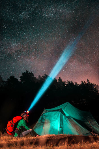 Woman sitting by tent on land at night