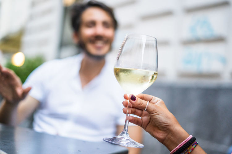 Cropped hand holding wineglass with man in background