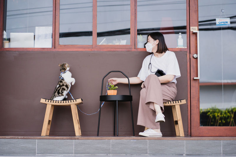 Asian woman wearing protective mask sit and play with her cat at outdoor coffee shop