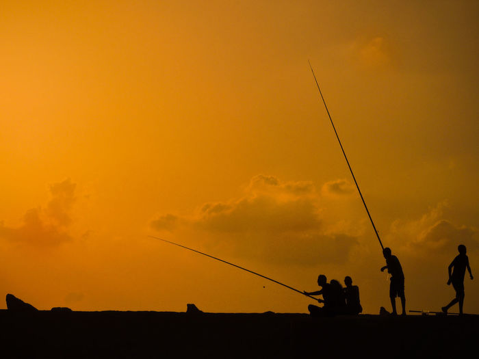 Silhouette people fishing against sky during sunset