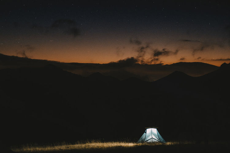 Tent on mountains against cloudy sky at sunrise