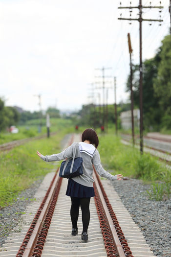 Rear view of woman in school uniform on railway tracks