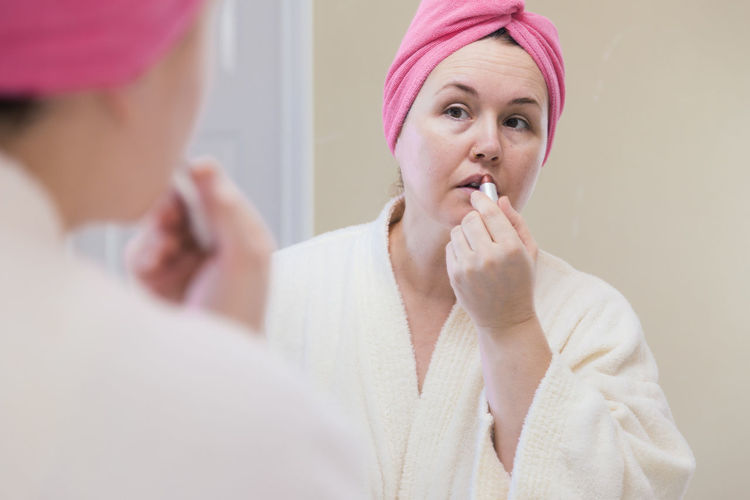 Mature woman applying lipstick reflecting on mirror