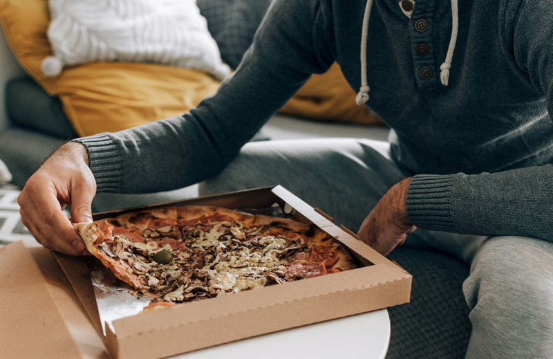Man sitting on couch, eating pizza. pizza box, pizza delivery.
