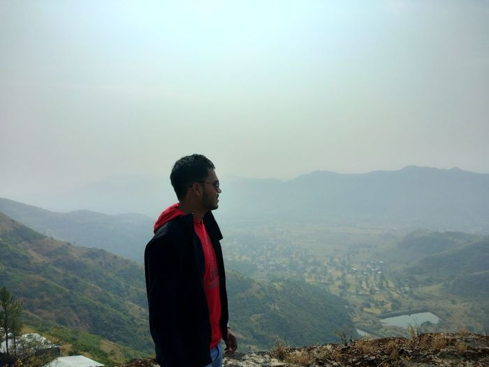 Young man looking at mountains against sky