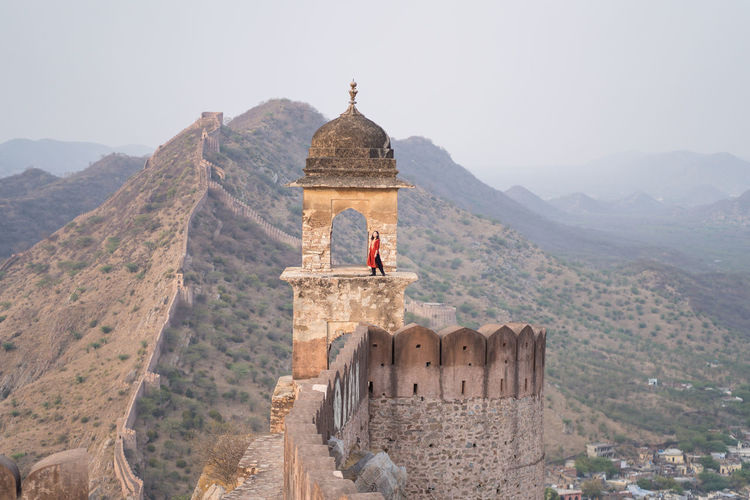 Full length woman standing in arch of old tower against mountain ridge and walls while visiting amer fort viewpoint in jaipur, india