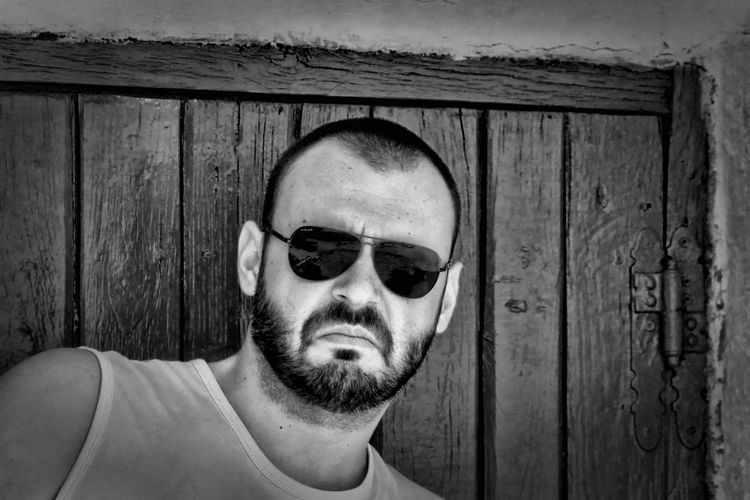 Portrait of serious man wearing sunglasses against wooden door