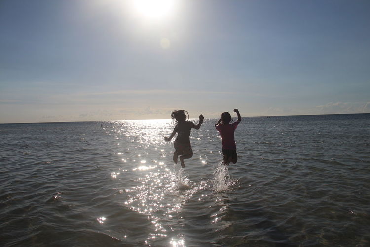 Rear view of girls jumping in sea against sky