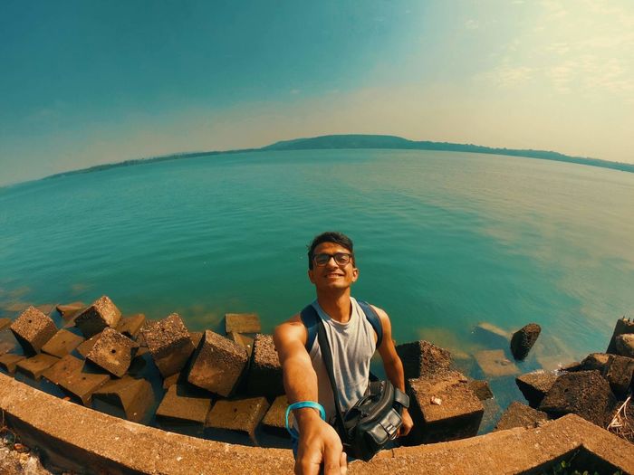 Portrait of young man sitting by sea against sky