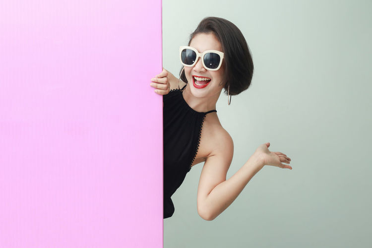 Portrait of young woman in sunglasses against pink background