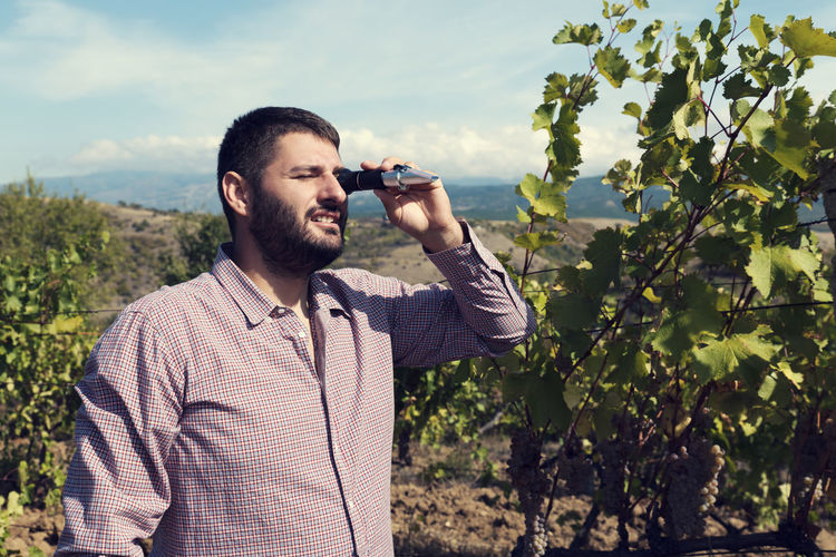 Man using refractometer while standing in vineyard against sky