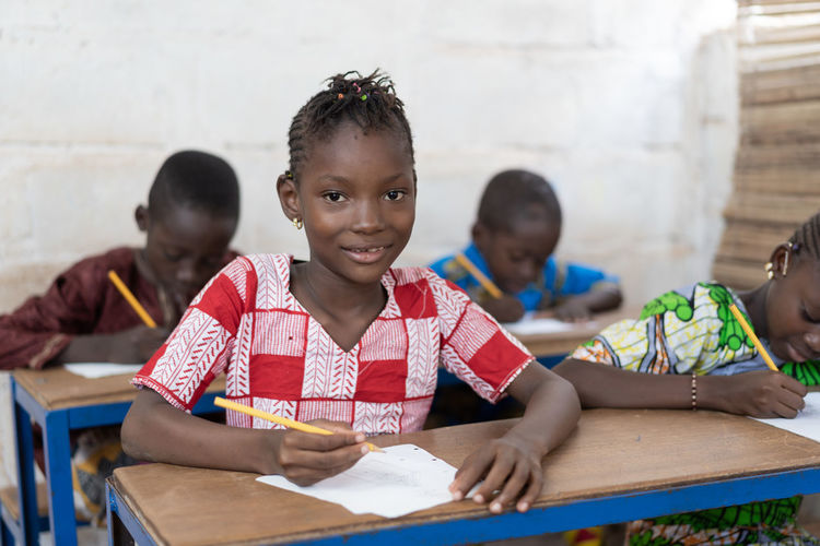 Portrait of girl writing at table in classroom