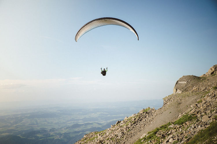View of man paragliding over landscape against sky