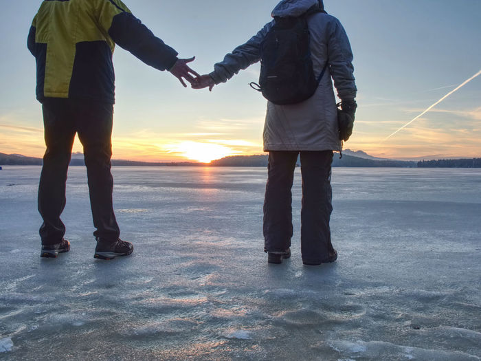 Couple has fun during winter walk on ice of frozen lake. evening hike. warm clothes with high boots