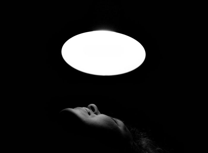 Young woman under illuminated pendant light in darkroom at night